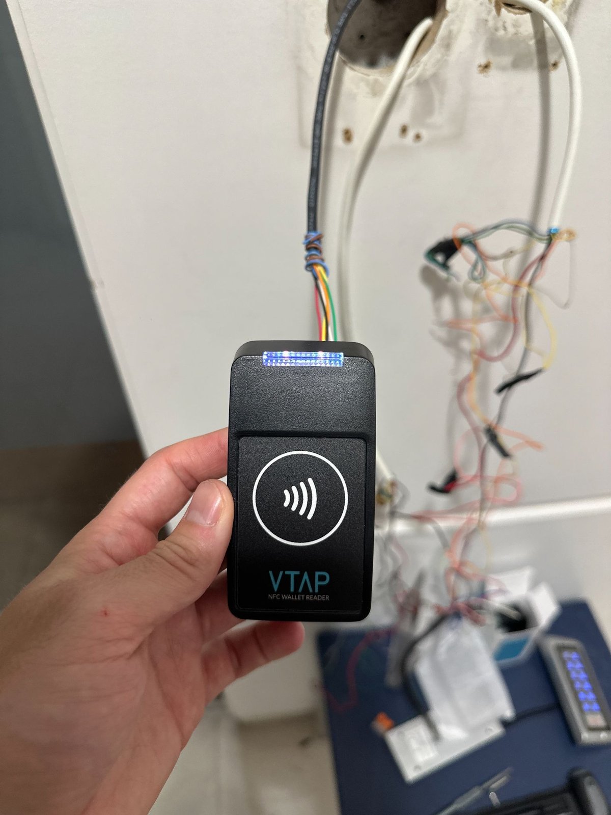 A VTAP NFC card reader held in front of the wiring it replaced